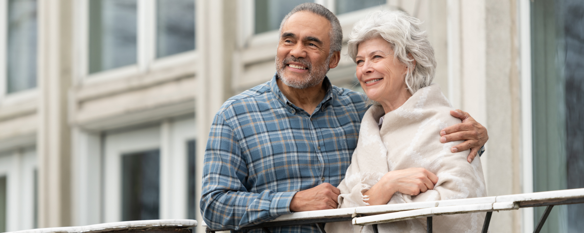 Elderly couple embracing and smiling from a balcony in the city