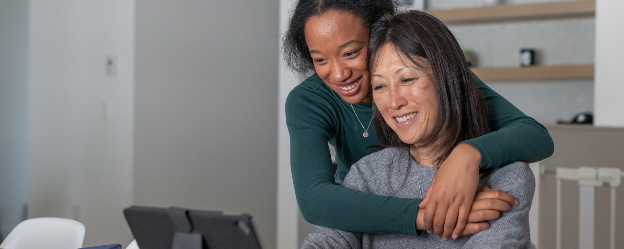 Mother and daughter embracing while smiling and looking at a tablet about her RESP