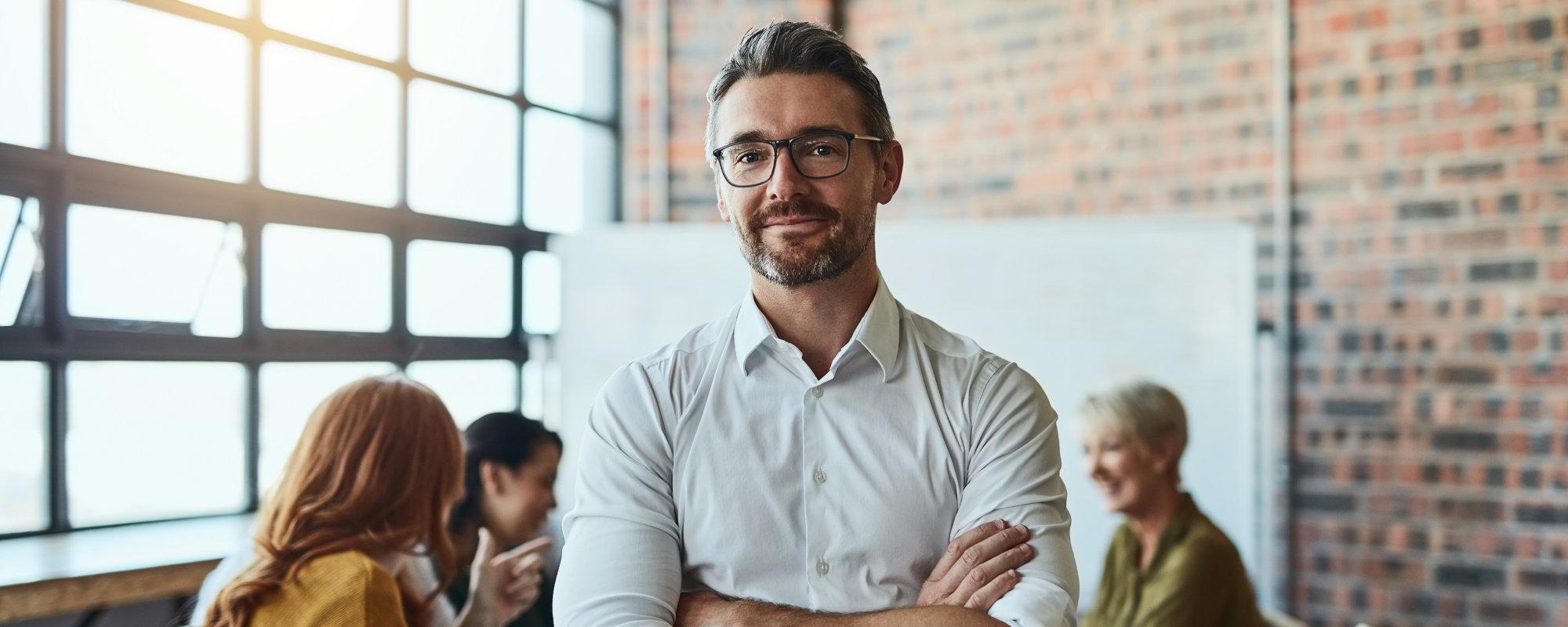 Man in a meeting room facing the camera crossing his arms