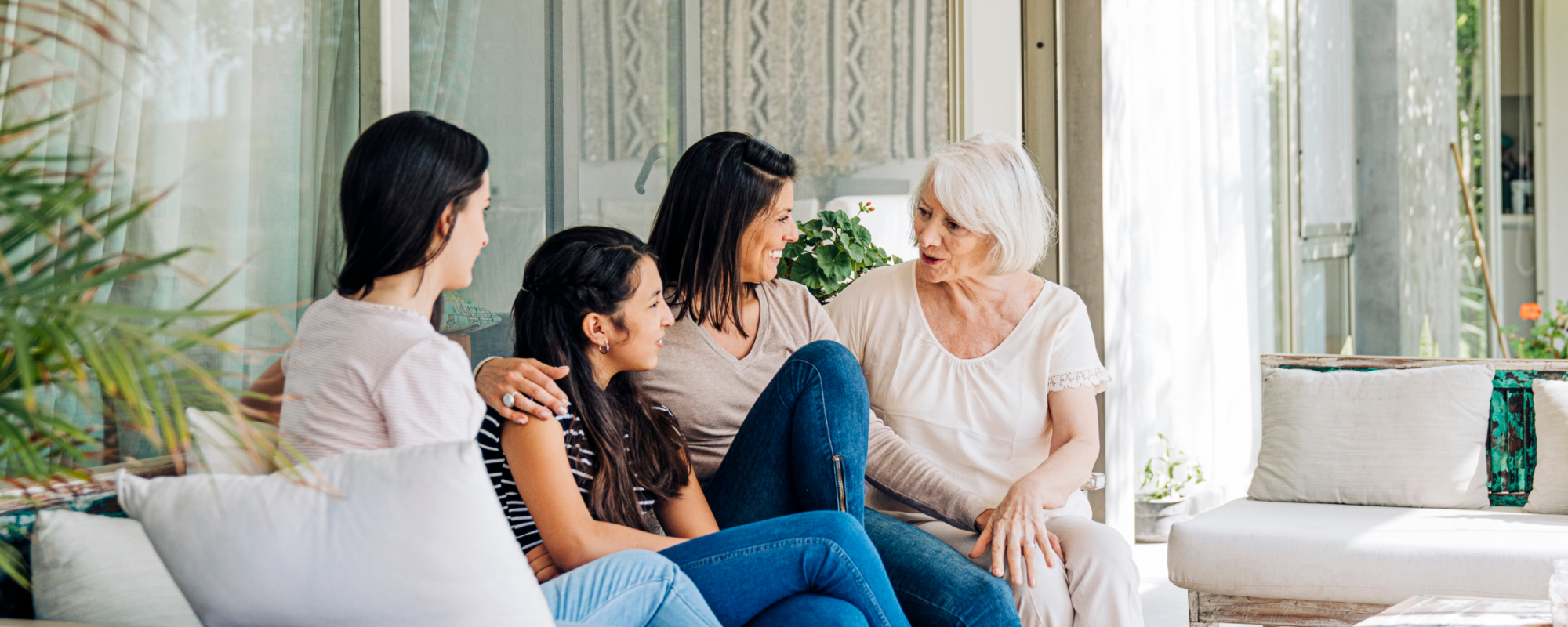 2 filles, une mère et une grand-mère assises sur un canapé-terrasse extérieur, se parlant et souriant