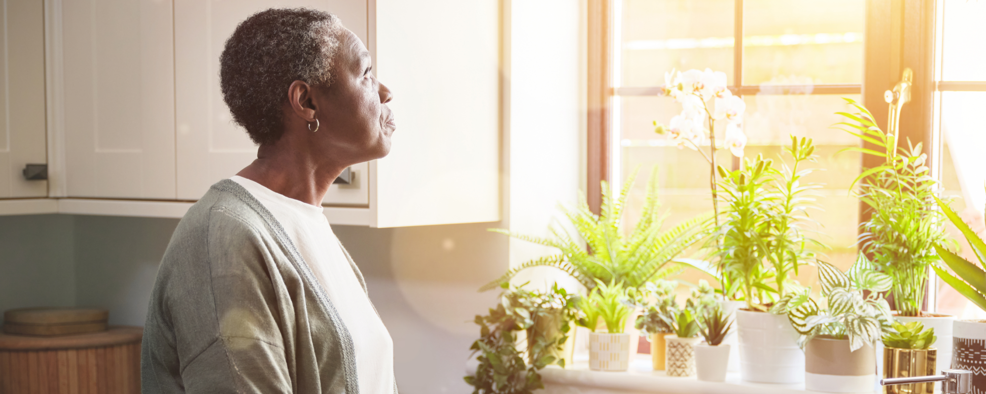 Femme regardant par la fenêtre de sa cuisine au soleil