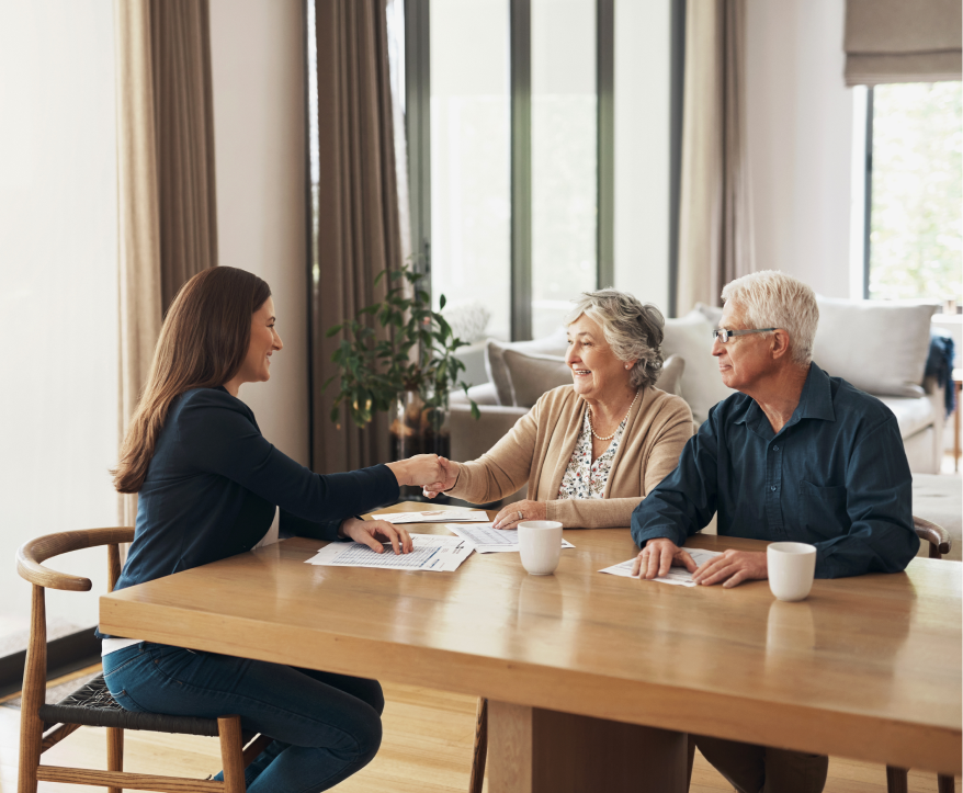 older couple sitting at table shaking hands with lady across the table