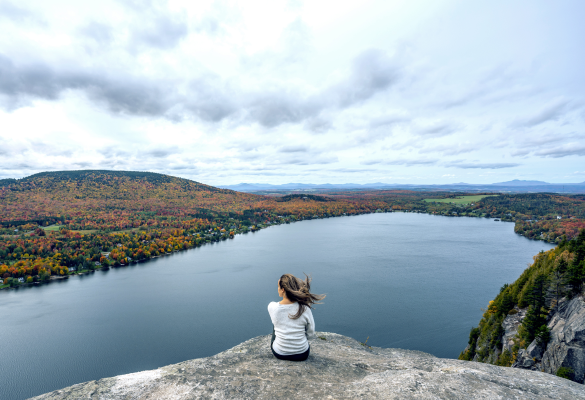 Woman sitting on cliff overlooking lake and trees in autumn