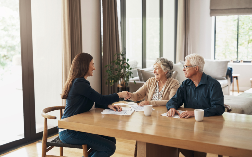 eldery couple sitting at table shaking hands with a lady sitting across from them