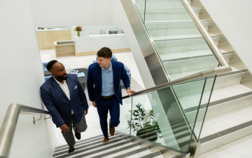 Two men in suits walk up glass stairs