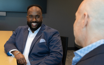A man smiles while speaking to someone sitting across from them