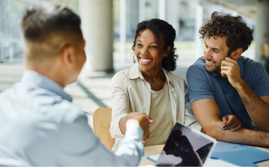 man and woman smile and shake hands with person across from them