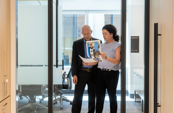 Two people stand in an office doorway looking over documents