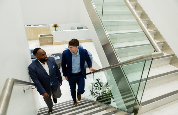 Two men in suits walk up glass stairs