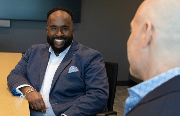 A man smiles while speaking to someone sitting across from them