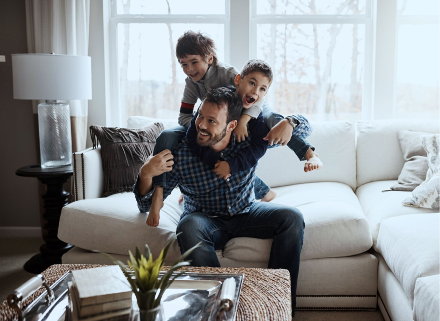 man and 2 boys play wrestling on a couch