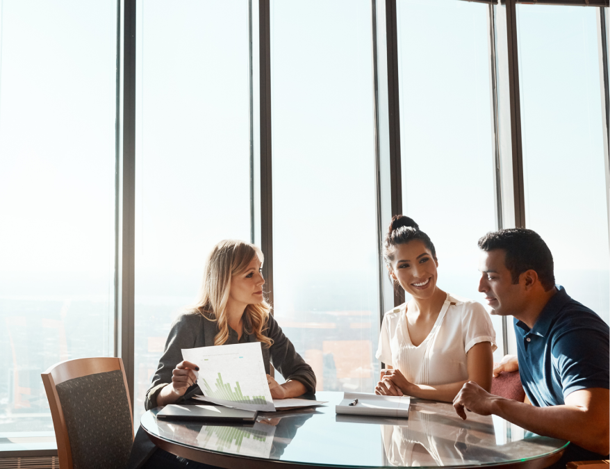 man and woman sitting at desk speaking to woman holding documents