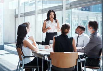 lady standing up talking to a group of people sitting around a table