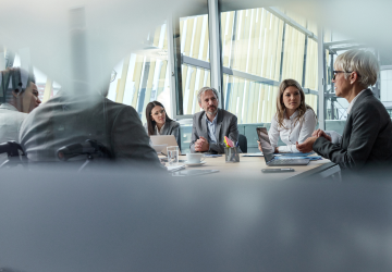 several people sitting in a board room listening to someone speak