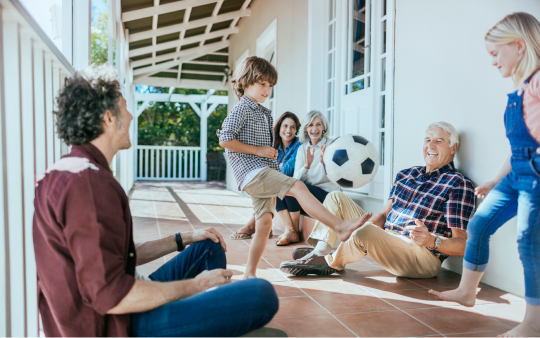 family of six sitting on porch watching kid kick soccer ball
