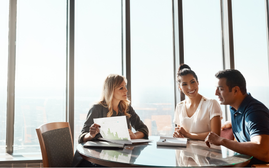 three people sit around a table looking at documents