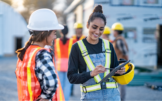 two women wearing bright orange vests and yellow hard hats