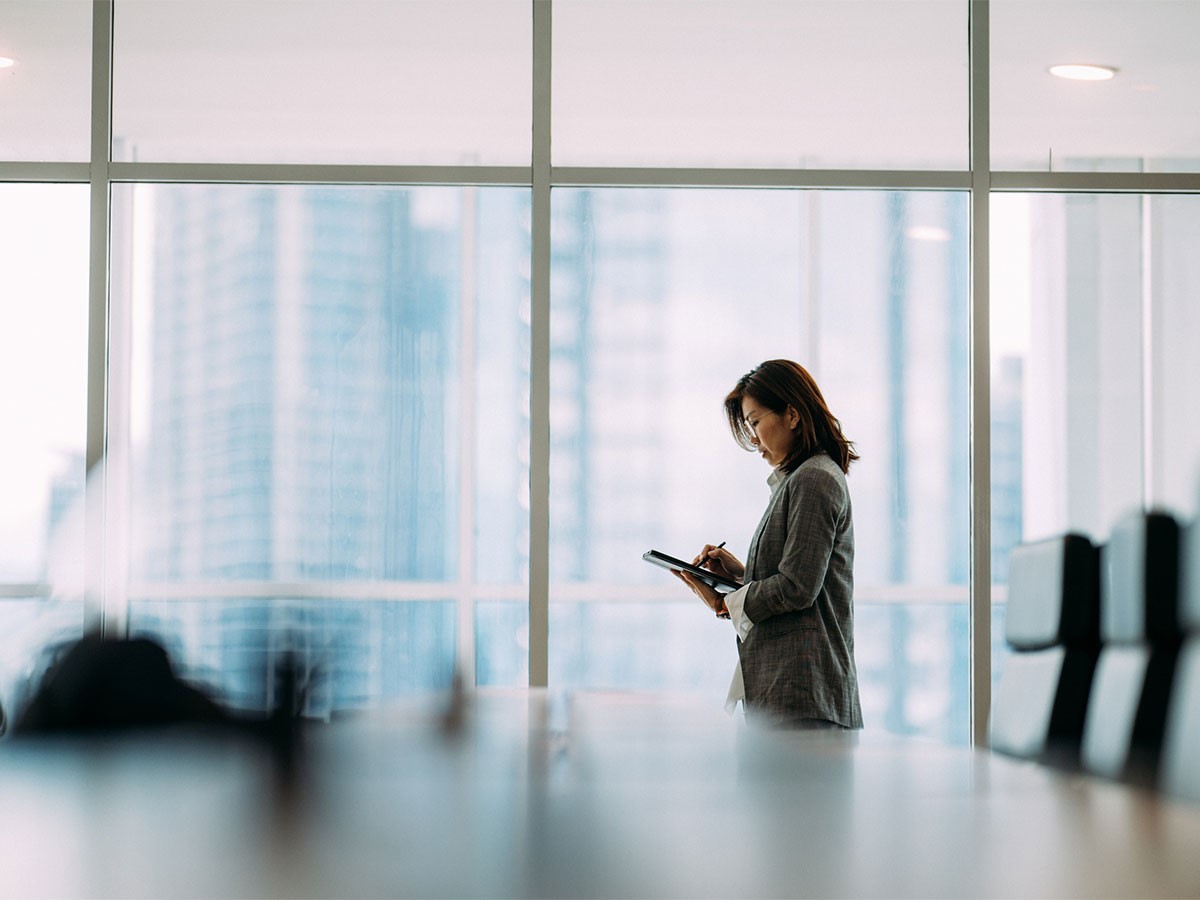 A business owner working on a tablet beside office windows.