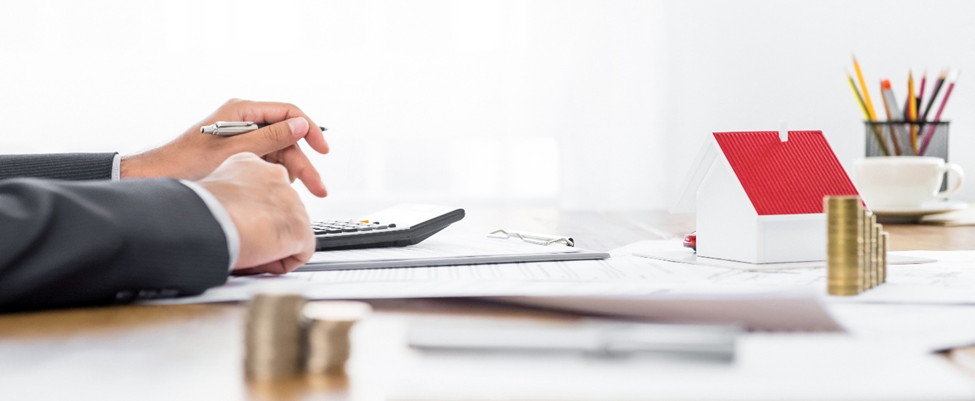 person in a suit's hands on a desk, holding a pen above a calculator and documents