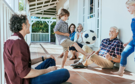 family sit on porch while young boy kicks soccer ball