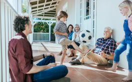 family sitting on porch watching kid kick soccer ball