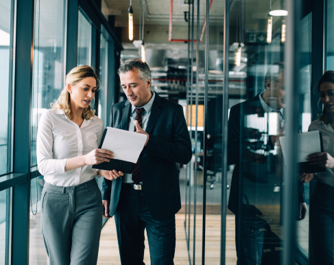 woman and man walking in office looking at papers