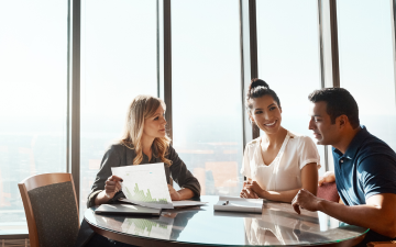 couple sitting at table speaking to lady holding chart