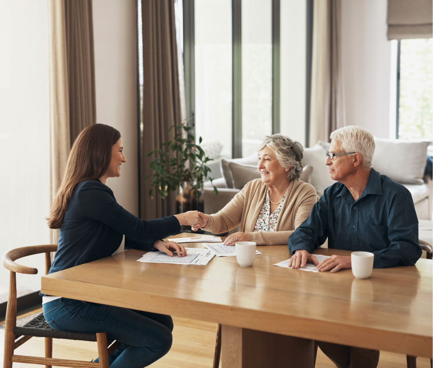 elderly couple sit at table shaking hands with a lady across from them