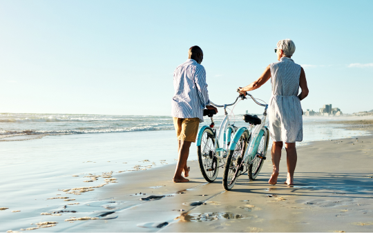 couple walk their bikes along the beach