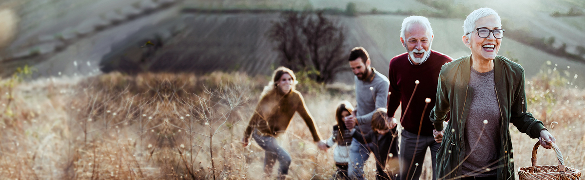 Two older adults at the forefront with couple and child in the background all walking in a field
